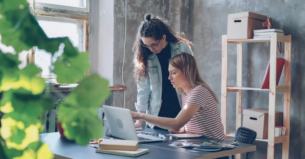 Deux jeunes femmes travaillant ensemble dans un bureau moderne avec un ordinateur portable et des plantes.