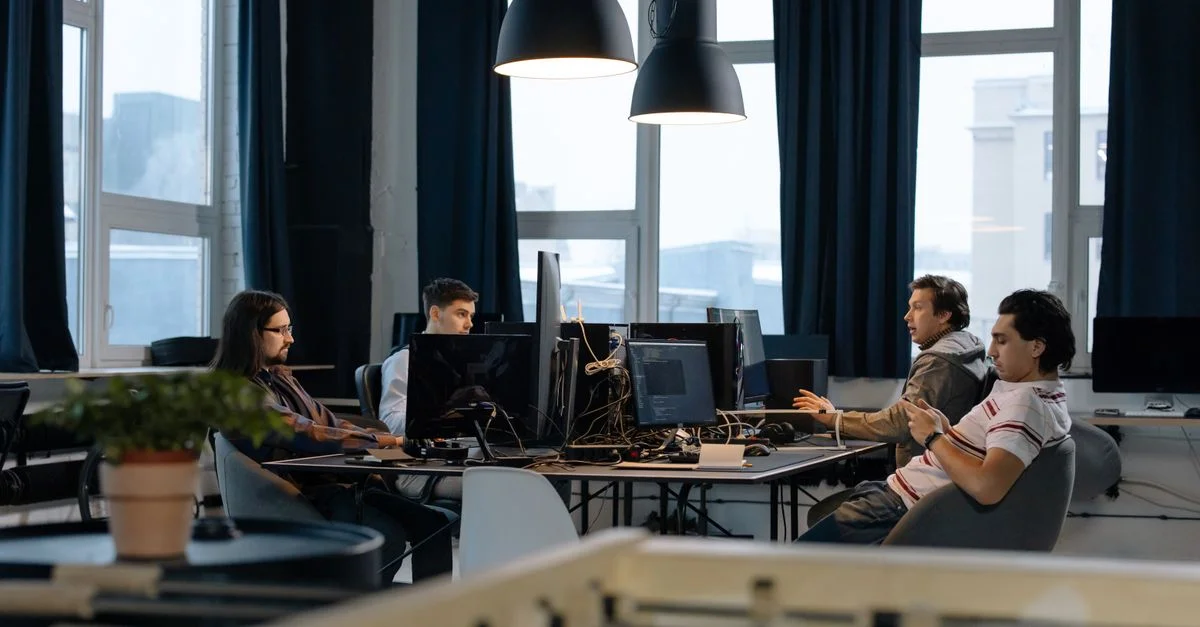 Des travailleurs collaborent dans un bureau moderne avec des ordinateurs, illustrant le travail d'équipe dans le développement technologique.