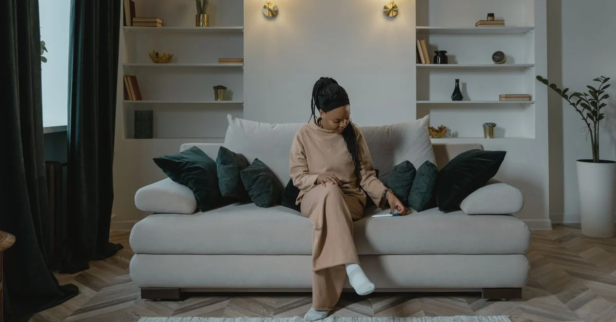 Une femme enceinte est assise pensivement sur un canapé dans un cadre de salon confortable.
