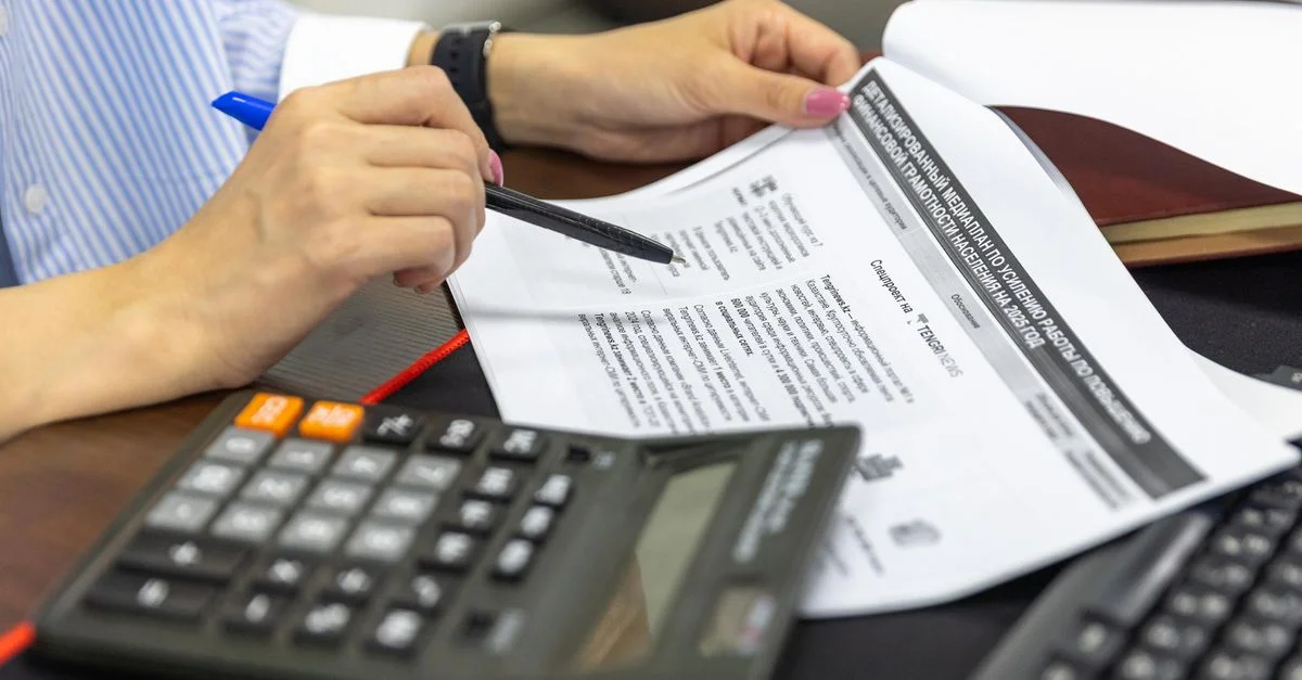 Gros plan sur une personne analysant des documents financiers à l'aide d'une calculatrice et d'un stylo.